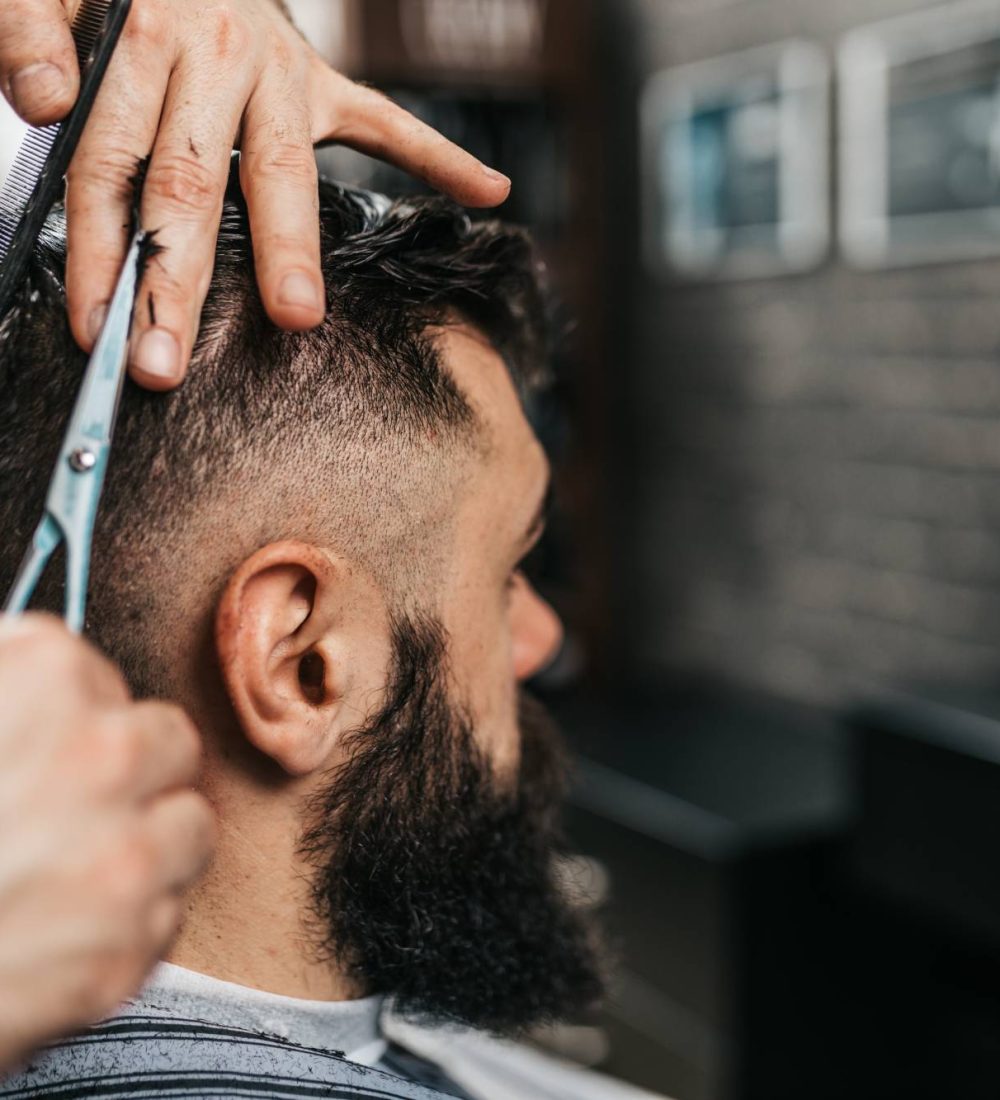 Good looking bearded man visiting hairstylist in barber shop.